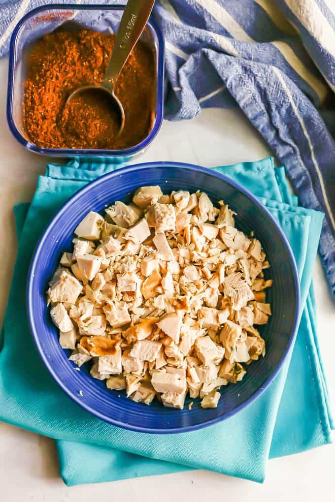 A blue bowl full of diced leftover Thanksgiving turkey on turquoise napkins and a container of homemade taco seasoning to the side