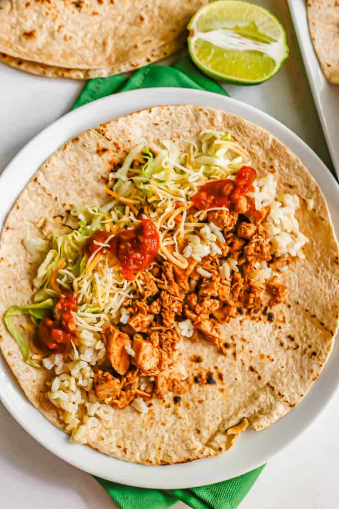 A whole wheat tortilla laid out on a white plate and loaded with brown rice, seasoned diced turkey breast, cheese, lettuce and salsa for a taco