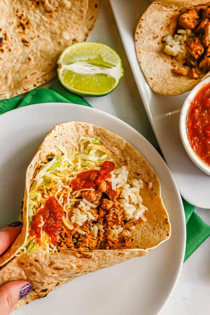 A hand folding up a soft shell taco with leftover turkey, rice, cheese, lettuce and salsa