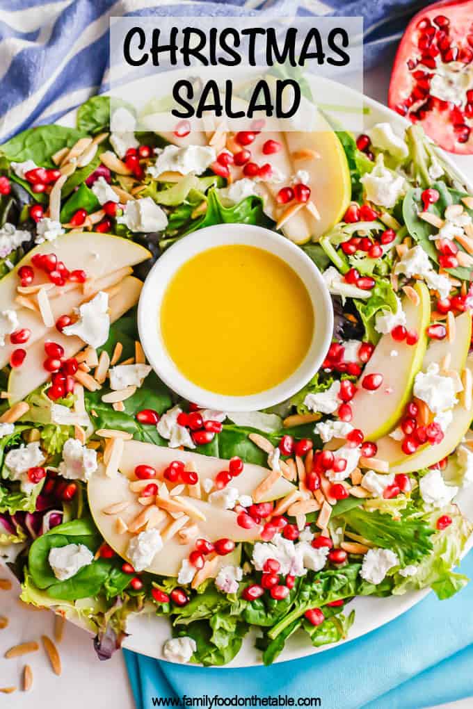 A white platter with a mixed greens salad with pears and pomegranates and a citrus dressing in the middle to look like a wreath with a text overlay on the photo