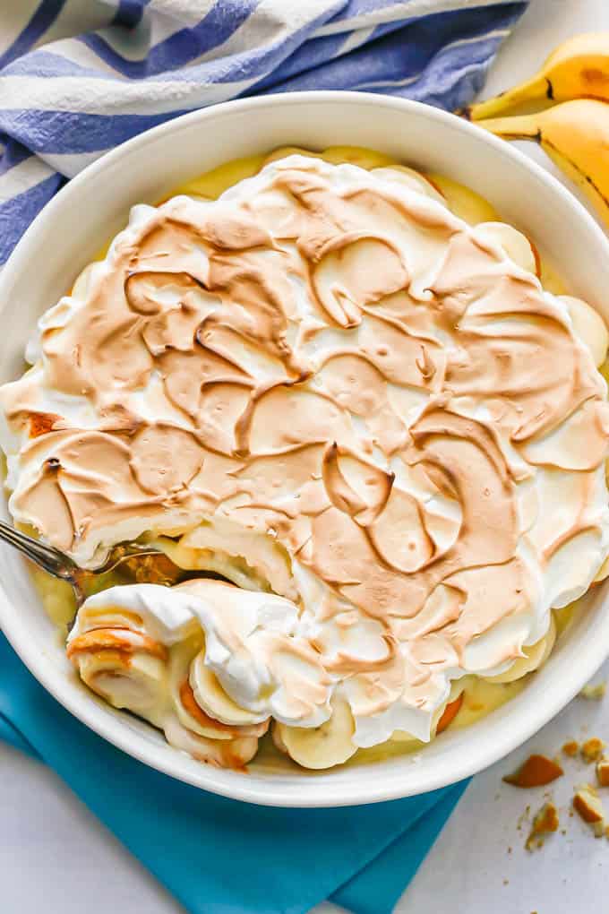 A large white round casserole dish with homemade banana pudding and meringue on top and a scoop being taken out