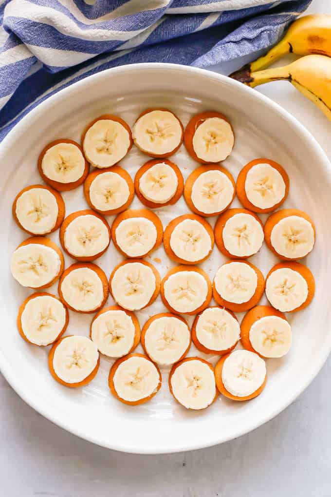 A white round casserole dish with Nilla wafers topped with sliced bananas