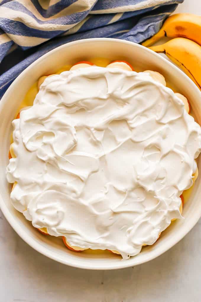 Meringue spread on top of custard, nilla wafers and banana slices layered in a large white casserole dish