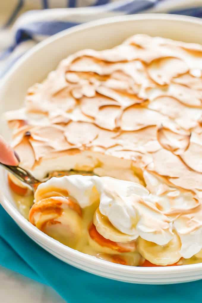 A spoon getting a scoop of banana pudding with meringue on top from a large white round casserole dish