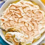 A large white round casserole dish with homemade banana pudding and meringue on top with a text overlay on the photo