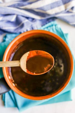 A wooden spoon lifting up a spoonful of chocolate sauce from a copper sauce pan