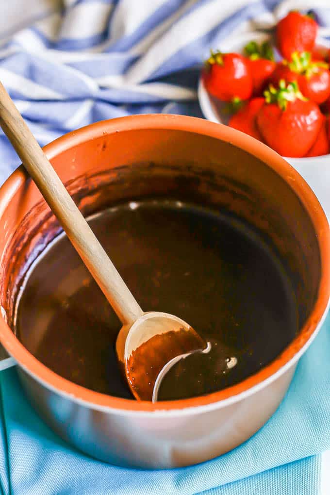 A wooden spoon resting in a small saucepan with homemade chocolate syrup
