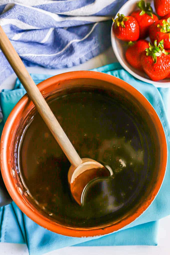 A small saucepan with homemade chocolate syrup and a wooden spoon resting in the pan