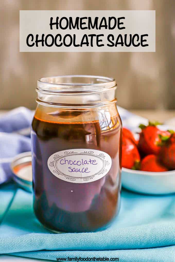 Chocolate sauce in a glass jar with a label and a bowl of strawberries in the background with a text overlay on the picture