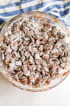 Muddy buddies with powdered sugar all mixed together in a large glass bowl