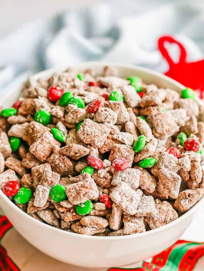 Reindeer chow served in a large white bowl with red and green Christmas ribbon twirling around it