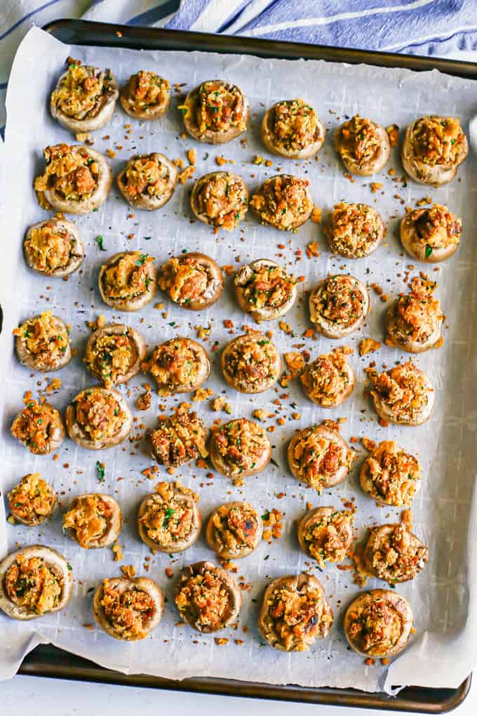 A parchment paper lined baking tray full of stuffed mushrooms after being baked in the oven