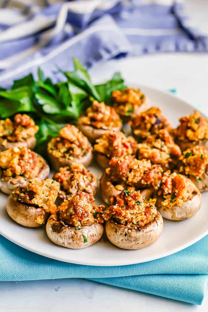 A round white plate with sausage stuffed mushrooms and a garnish of fresh parsley