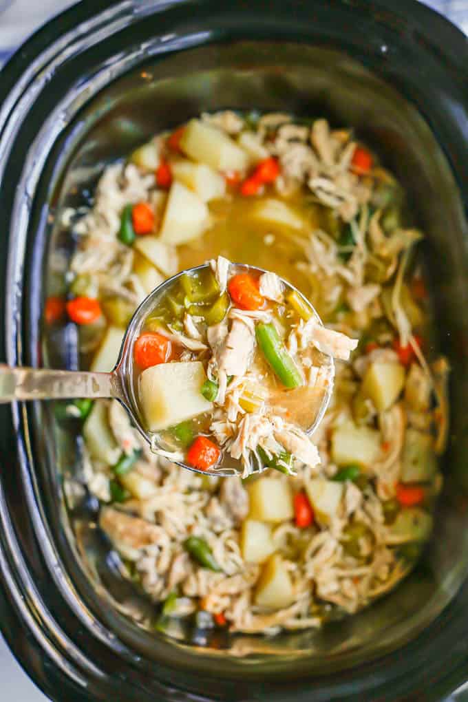 A ladle of chicken stew being lifted from a slow cooker