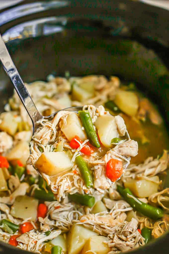 A ladle of chicken stew being lifted up from a crock pot