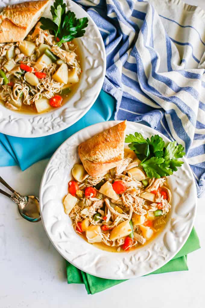 Two bowls of chicken stew served with parsley and big hunks of bread