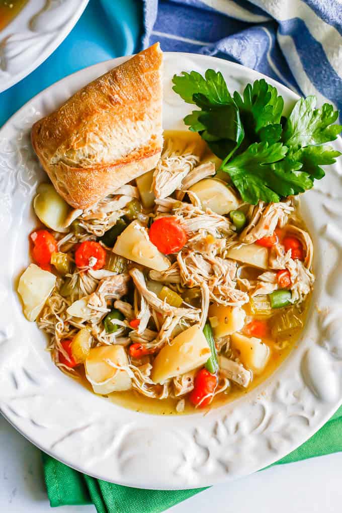 Chicken stew with potatoes, carrots and green beans served in a white soup bowl with parsley and a hunk of bread