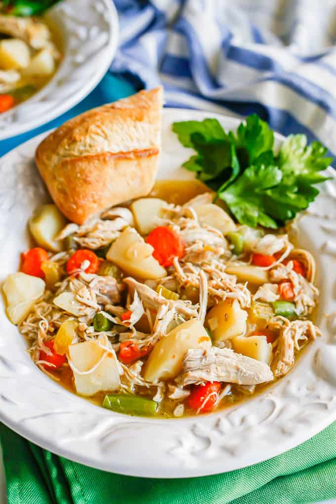 A white bowl with chunky chicken stew with parsley and a hunk of bread