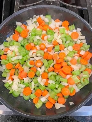 A large skillet with sautéed onion, celery and carrots