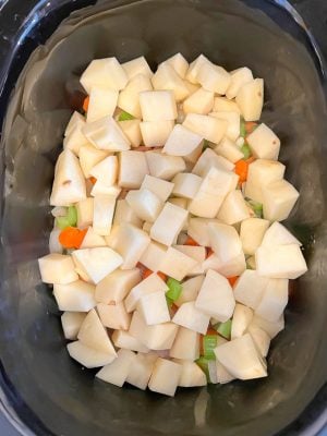 Cubed potatoes on top of other veggies in a slow cooker before being cooked