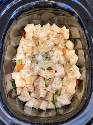 Seasonings on top of cubed potatoes and other veggies in a slow cooker