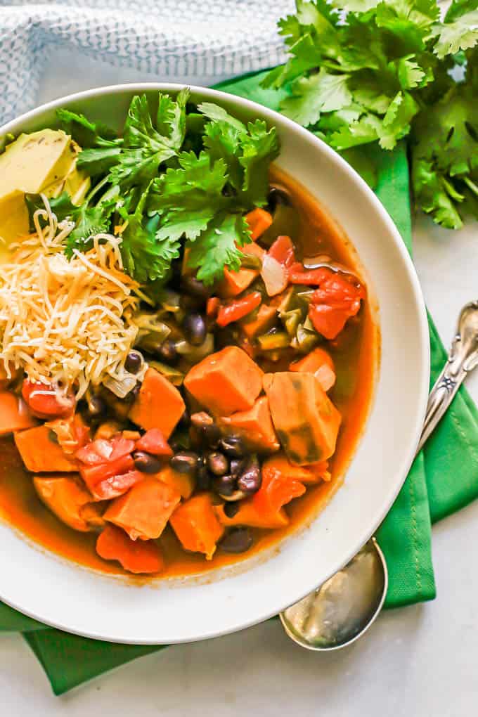 Overhead shot of sweet potato chili in a white serving bowl with toppings and a spoon on green napkins to the side