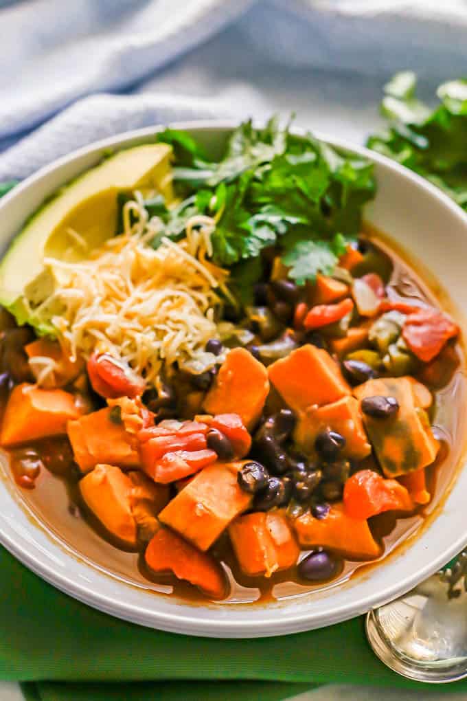 Vegetarian chili in a low white bowl with shredded cheese, avocado and cilantro on top