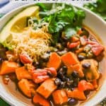 A low white bowl of sweet potato and black bean chili with toppings and a text overlay on the photo