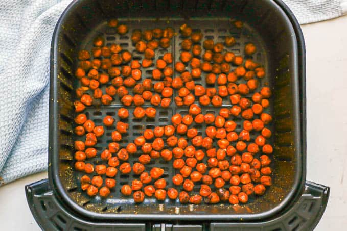 Seasoned and cooked, crispy chickpeas in an Air Fryer tray with a light blue towel nearby