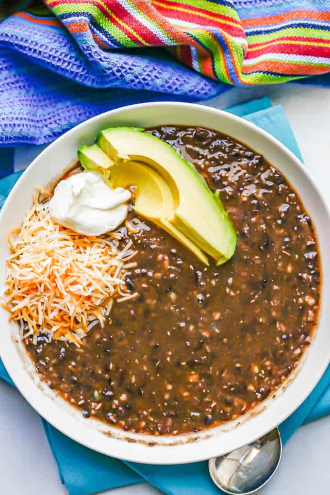 A low white bowl with black bean soup topped with shredded cheese, sour cream and avocado