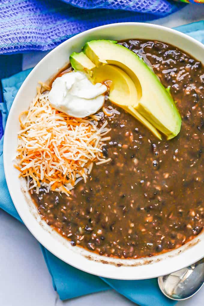 Close up of a white bowl filled with black bean soup topped with cheese, sour cream and avocado slices