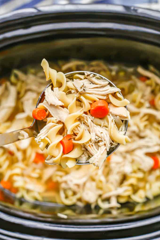 A ladle of chicken noodle soup being lifted from a slow cooker