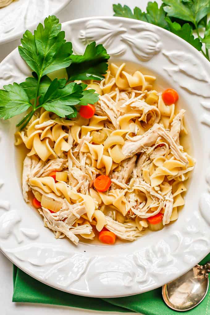 Chicken noodle soup served in a low white soup bowl with sprigs of parsley to the side