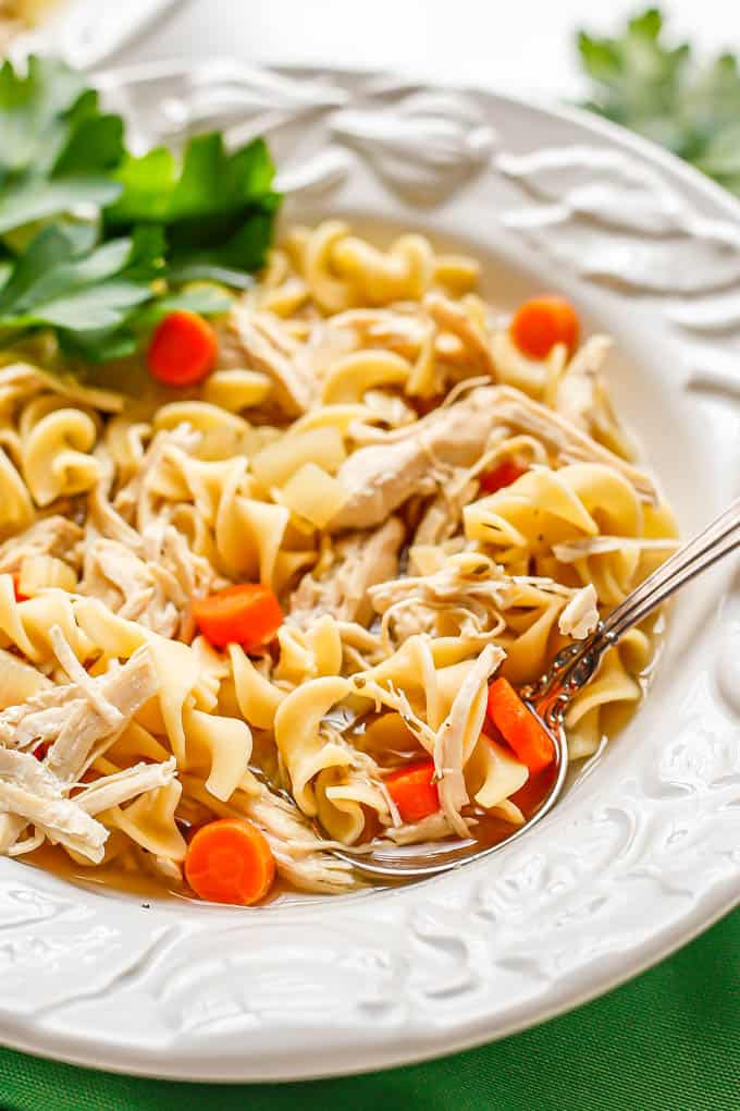 A spoon resting in a low white serving bowl of chicken noodle soup