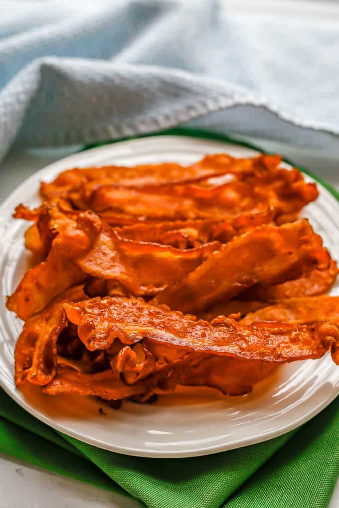Cooked strips of bacon piled up on a small white plate set on green napkins