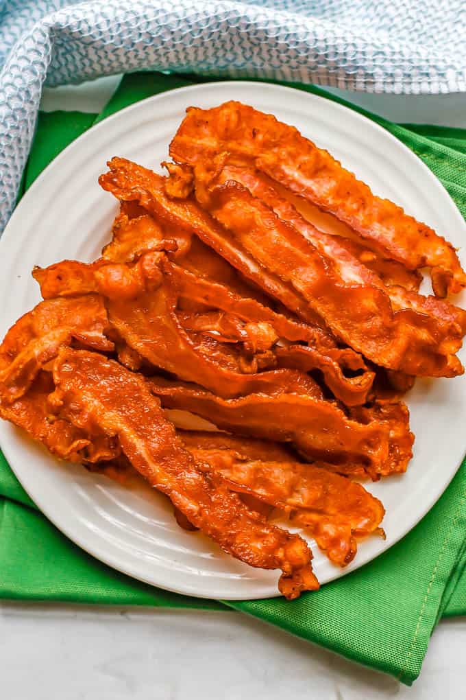 Overhead shot of cooked strips of bacon piled up on a small white plate set on green napkins