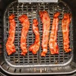 Strips of cooked, crispy bacon in an Air Fryer tray with a text overlay on the photo