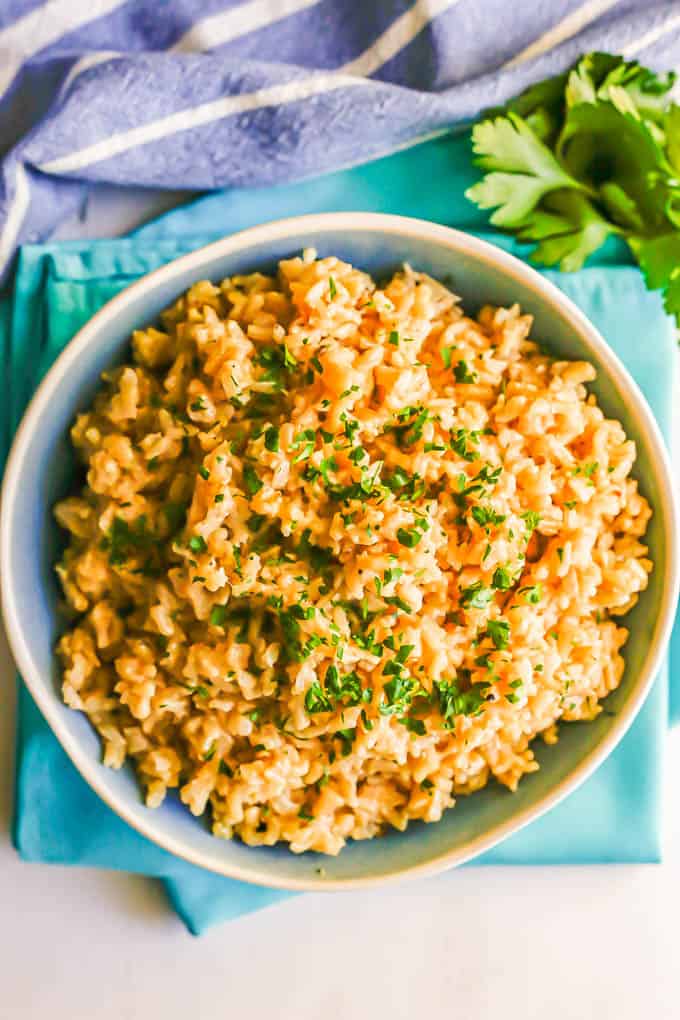 A serving bowl of rice pilaf with parsley on top set on turquoise napkins