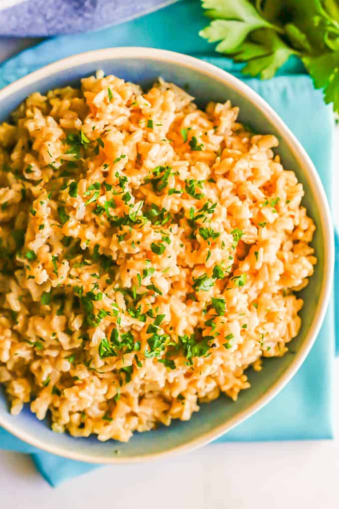 Close up of brown rice parsley in a large serving bowl with parsley sprinkled on top and some parsley sprigs to the side