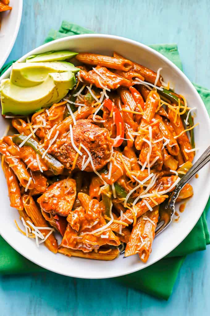 A fork resting in a low white bowl of fajita pasta with chicken set on green napkins