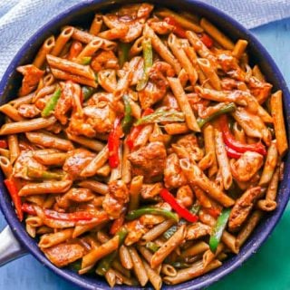 A fajita chicken and pasta mixture after being cooked in a large skillet with green and blue napkins nearby