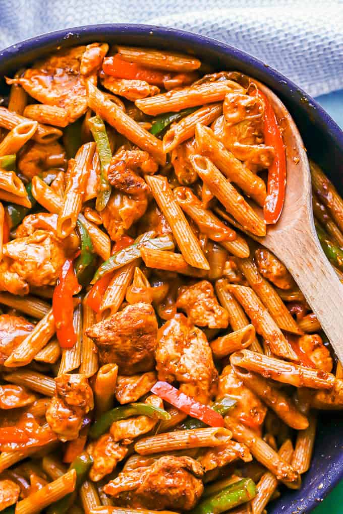 A wooden spoon resting in a skillet with fajita chicken pasta