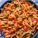A large skillet of fajita chicken pasta with peppers and onions and a text overlay on the photo