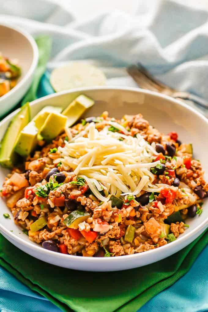 A ground turkey and rice dinner with beans and veggies served in a white bowl with cheese and avocado