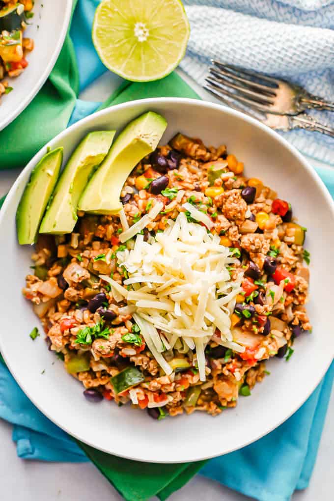 Close up of a ground turkey, rice, beans and veggie mixture served in a low white bowl and topped with cheese and avocado slices