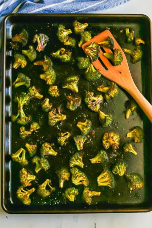 Browned oven baked broccoli on a sheet pan with a wooden spatula
