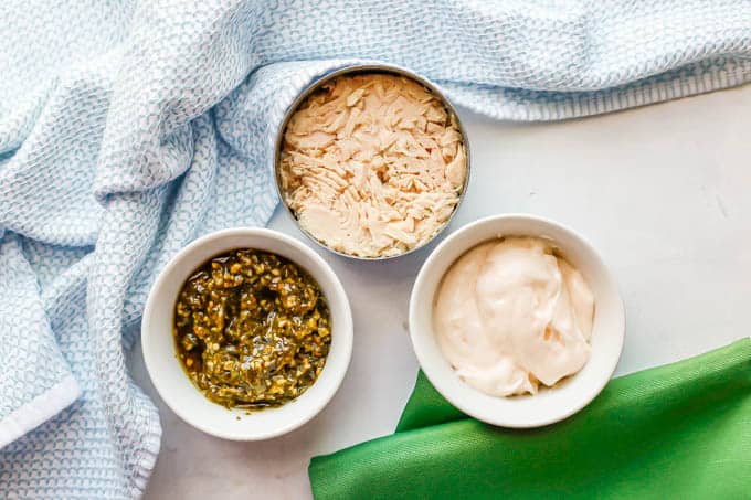 A can of tuna and bowls of pesto and mayonnaise laid out on a white marble countertop