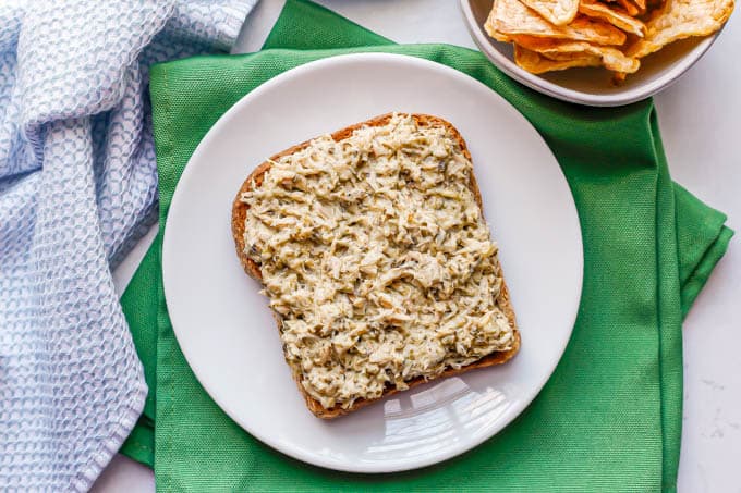 Tuna salad spread on a piece of whole grain toast on a small white plate