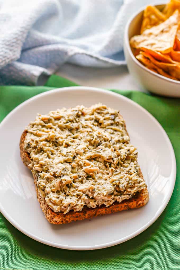 A small white plate with a piece of whole grain toast topped with pesto tuna salad