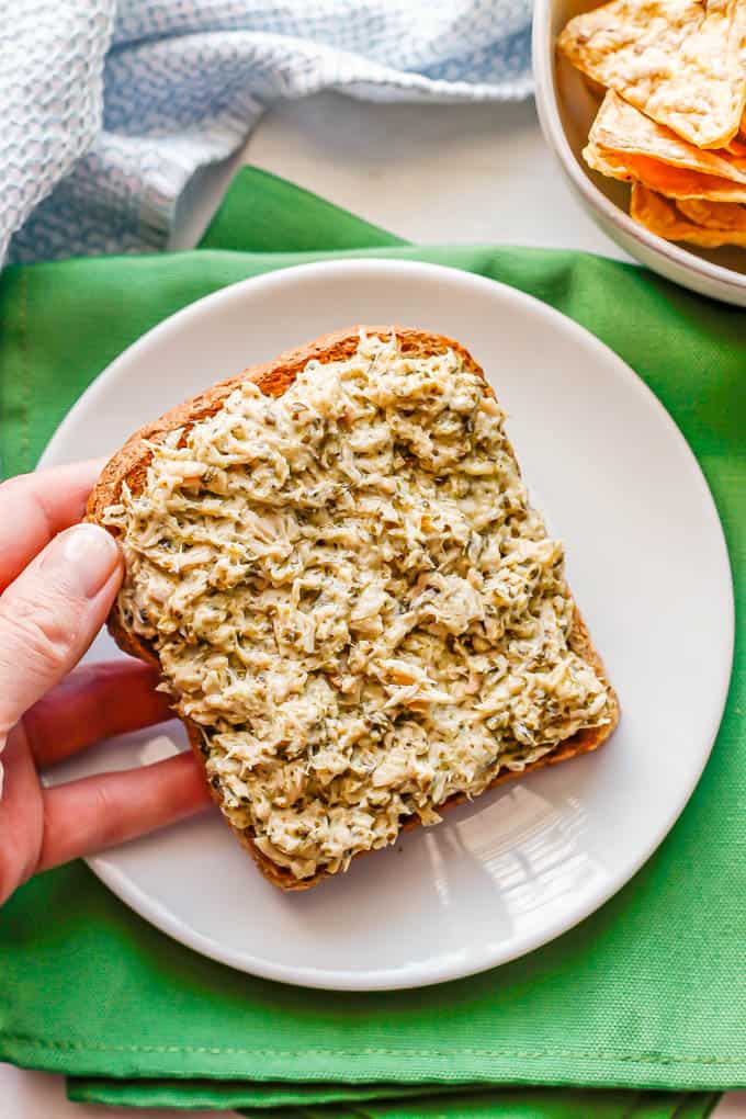 A hand holding a piece of toast with pesto tuna salad spread on it